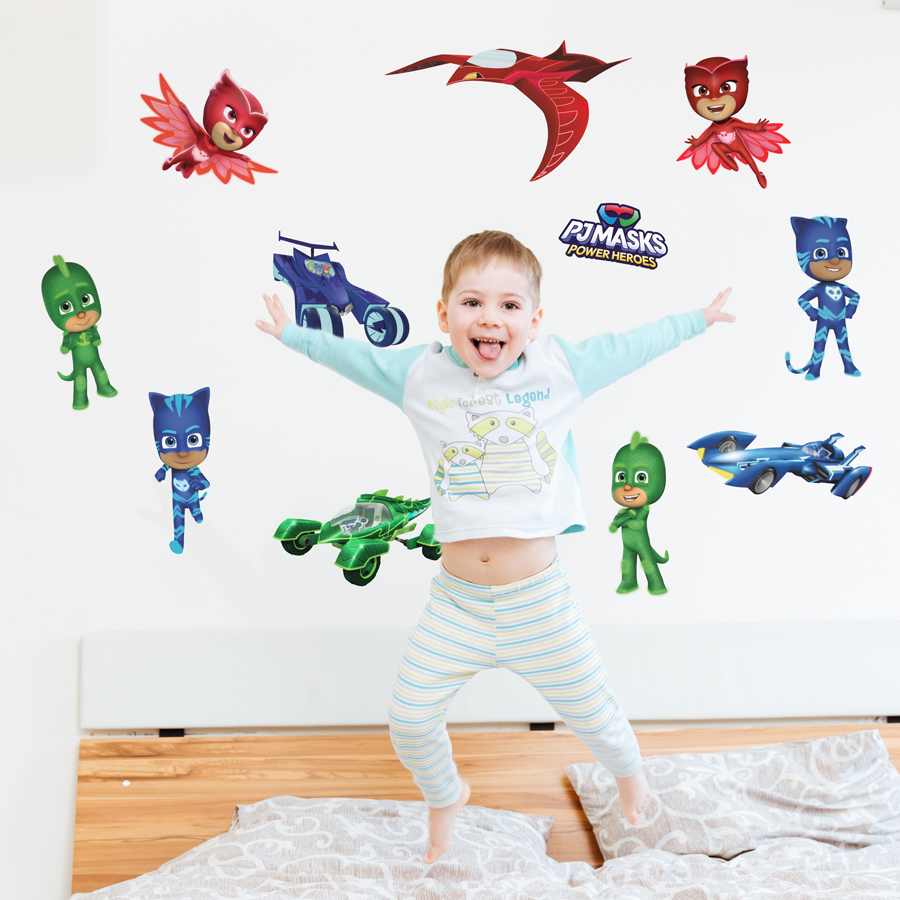 PJ Masks & vehicles wall sticker pack shown in a bedroom above a headboard with a child bouncing on the bed