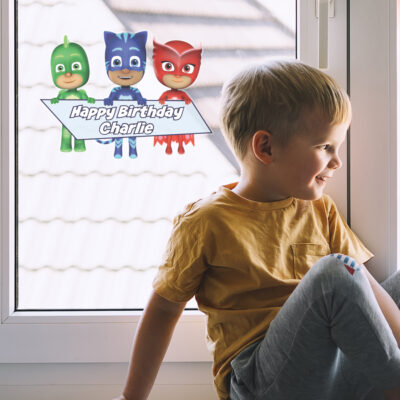 PJ Masks birthday window sticker shown on a window behind a boy