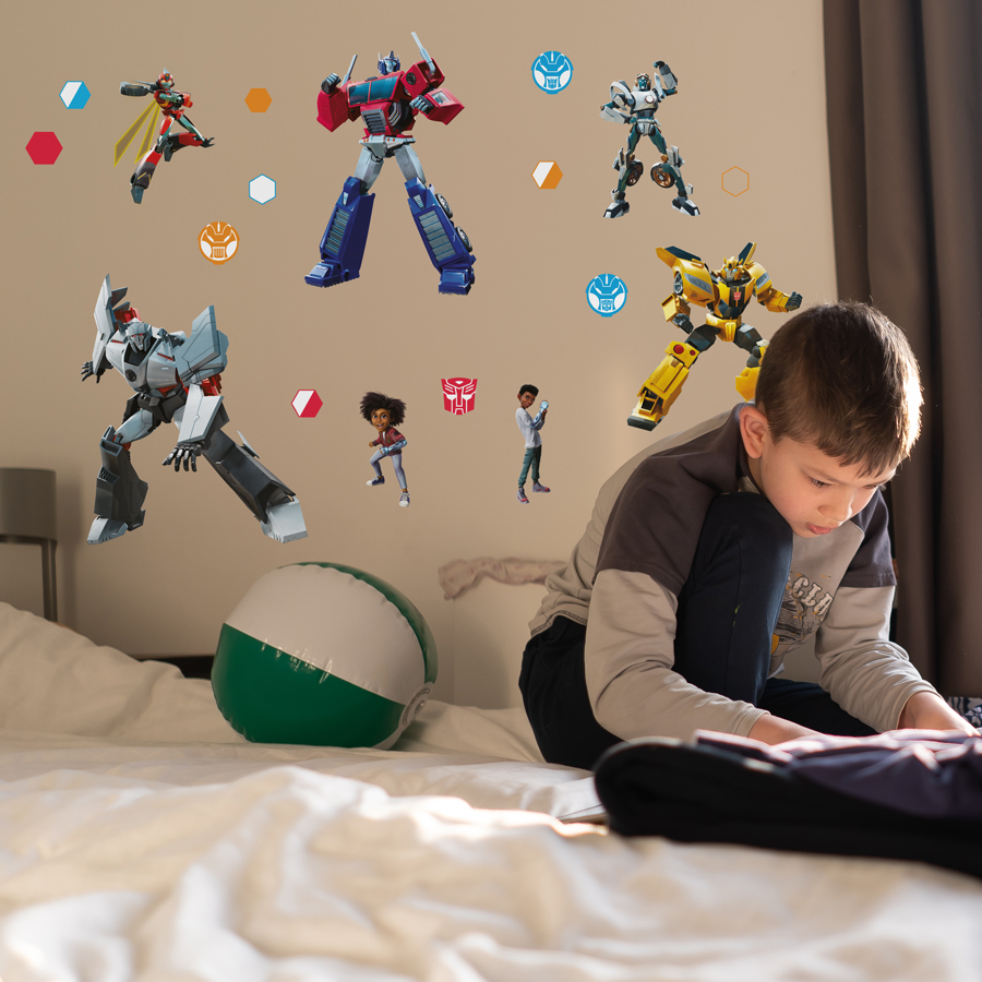 Transformers Earthspark wall sticker pack regular shown on a light brown wall behind a child reading on a white bed
