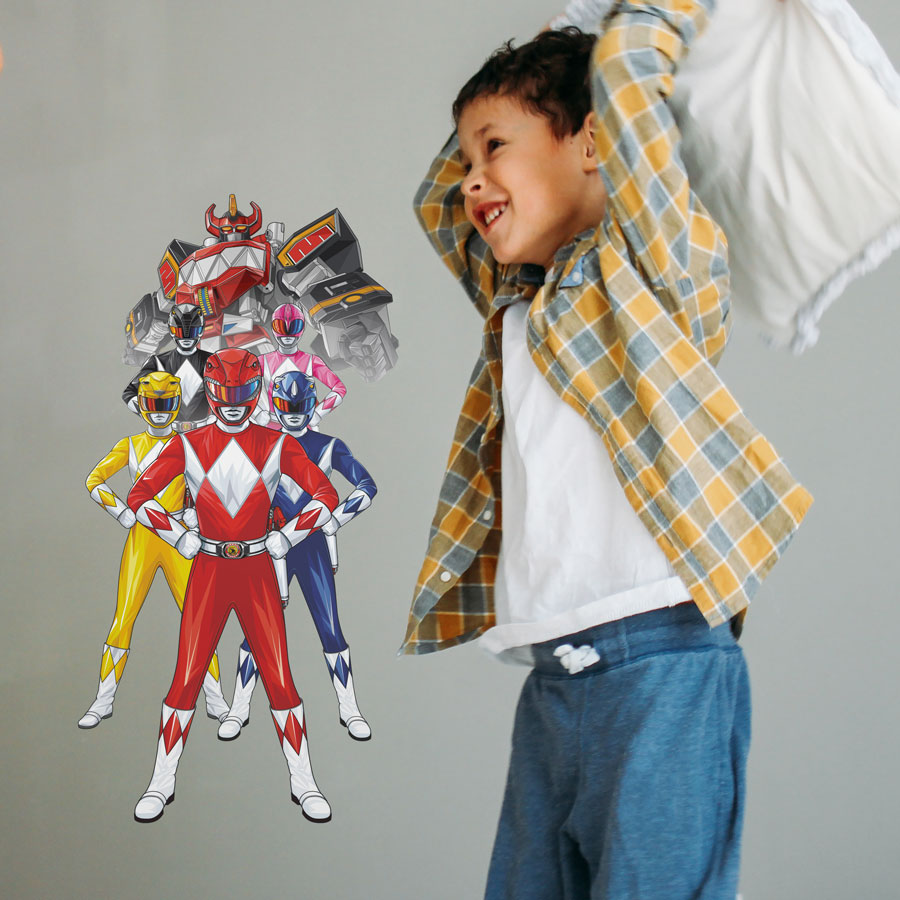 Power Rangers group wall sticker regular on a light grey wall behind a child throwing a white pillow
