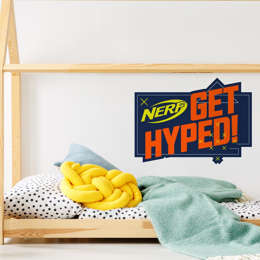 Get Hyped! Nerf wall sticker large shown on a white wall behind a light wood bed with white and black spotted bedding with blue and yellow pillows and blankets