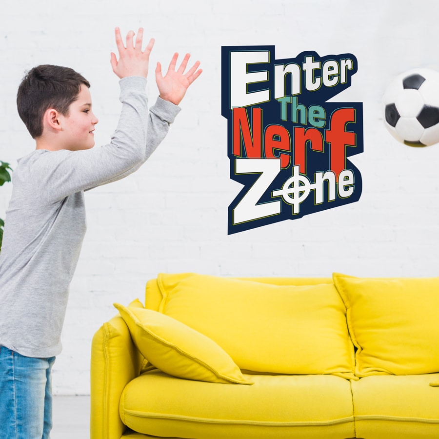 Enter The Nerf Zone wall sticker shown on a white wall behind a yellow sofa with a boy throwing a football