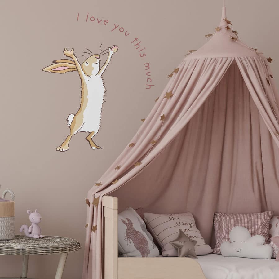 I love you this much wall sticker large shown on a pastel pink wall behind a light wood and pastel pink bed and side table