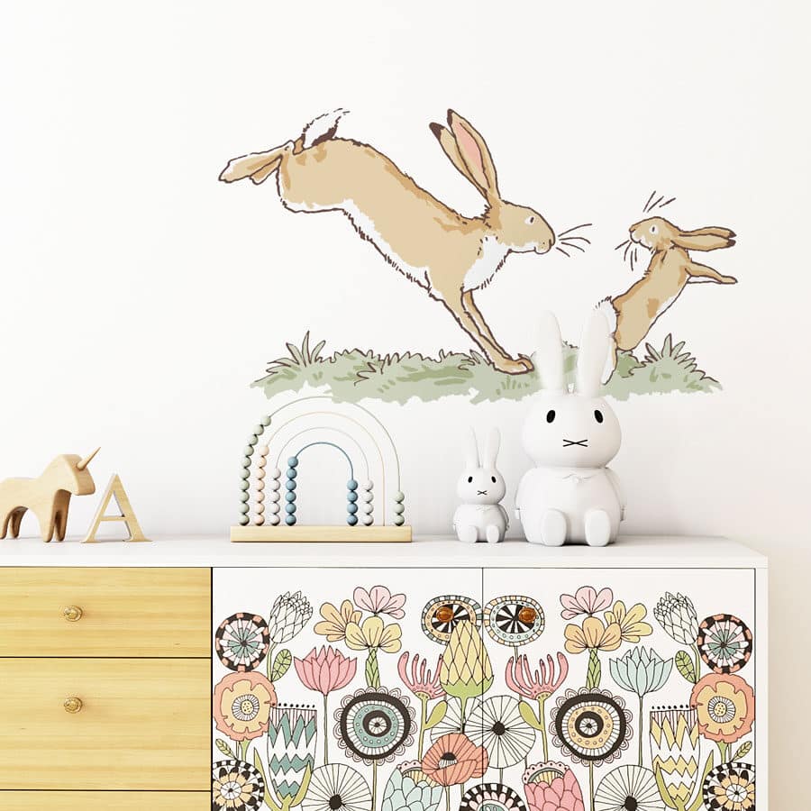 Leaping hares wall sticker shown on a white wall behind a floral painted wooden dresser