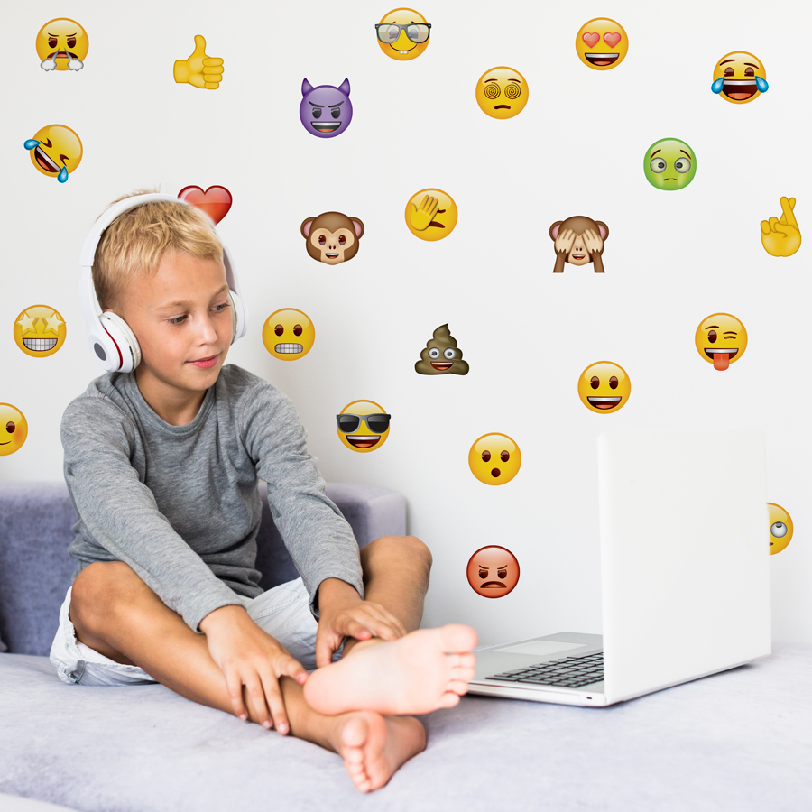 Mixed emoji wall sticker pack regular shown on a white wall behind a child watching a laptop