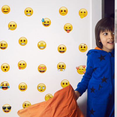 emoji Faces Wall Sticker Pack regular shown on a white wall behind a child dressed in blue with an orange blanket