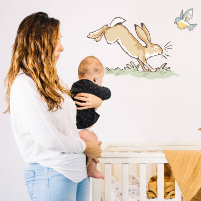 Hopping hare wall sticker shown on a white wall behind a woman holding a baby