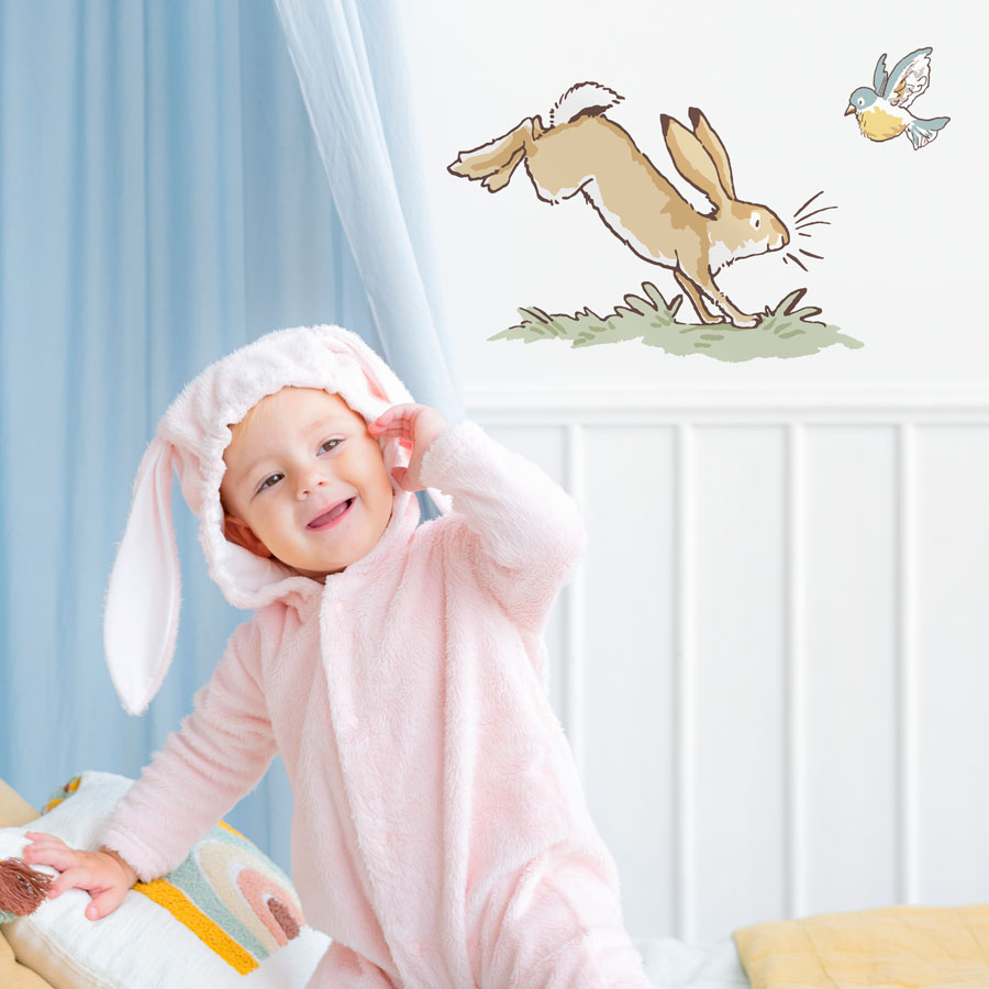 Hopping hare wall sticker shown on a white wall behind a toddler dressed as a rabbit