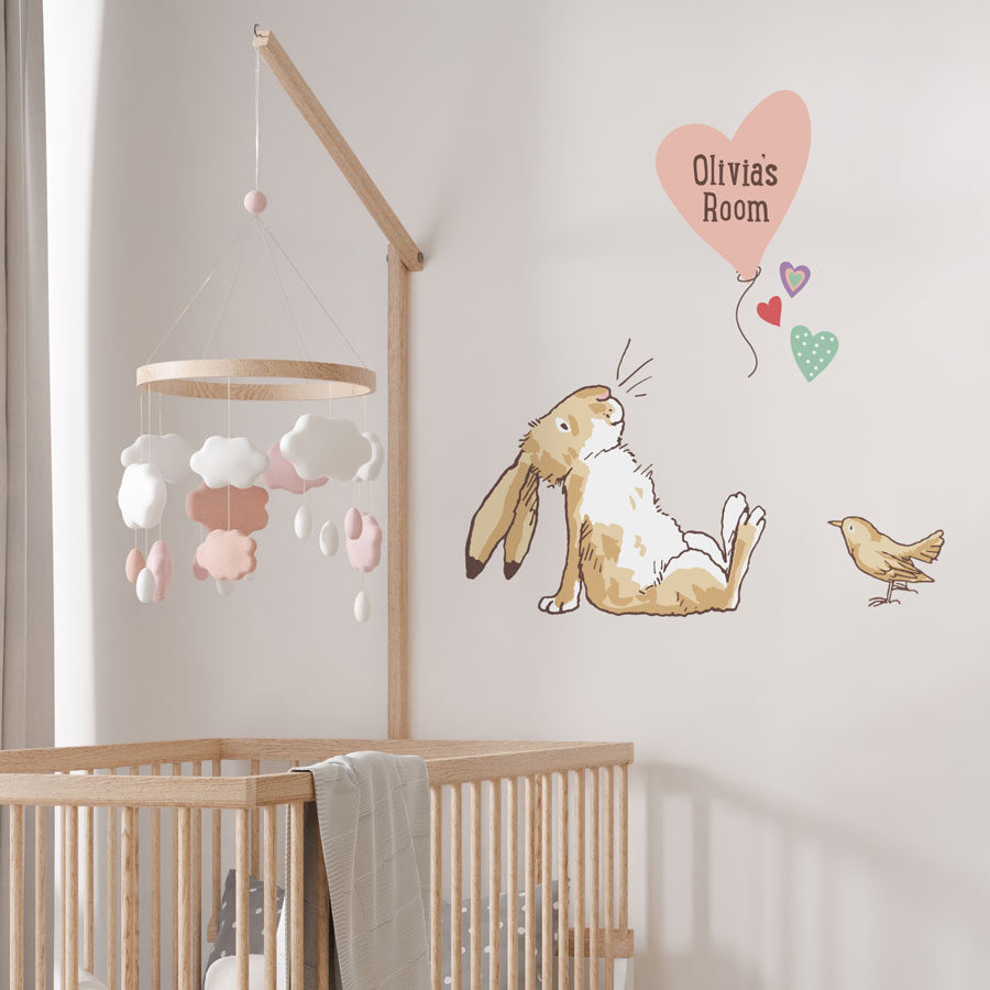 Personalised hare & balloon wall sticker on a white wall behind a wooden cot with a pink and white mobile