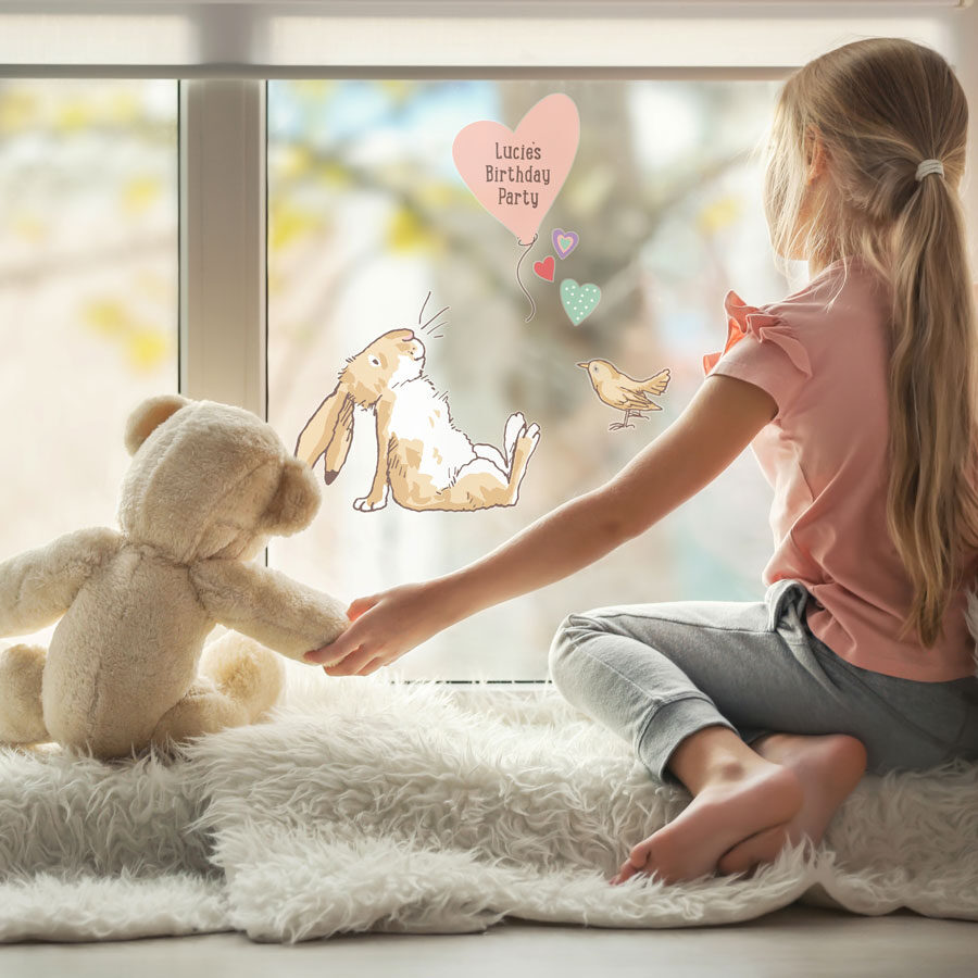 Personalised hare & balloon window sticker on a window behind a young child with a teddy bear looking outward