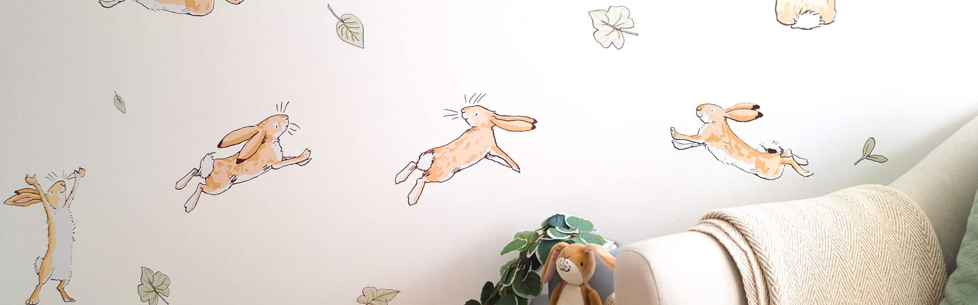 hero image of guess how much I love you wall stickers on a nursery wall with bunnies leaping and green leaves