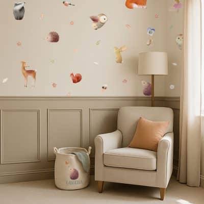 Cosy nursery corner with woodland wall stickers on a cream wall above a reading chair, styled with a personalised storage basket and soft tones.