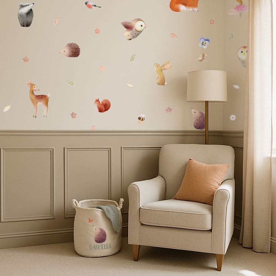 Cosy nursery corner with woodland wall stickers on a cream wall above a reading chair, styled with a personalised storage basket and soft tones.
