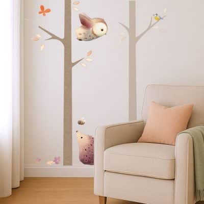 Neutral nursery corner with woodland tree wall stickers showing owl, bird, hedgehog and bees next to an armchair.