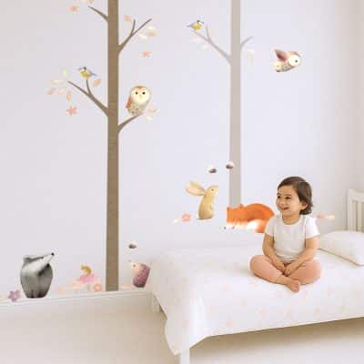 Nursery with woodland wall stickers showing animals and trees from Ginger Betty's Core Pack, with child sitting on bed.