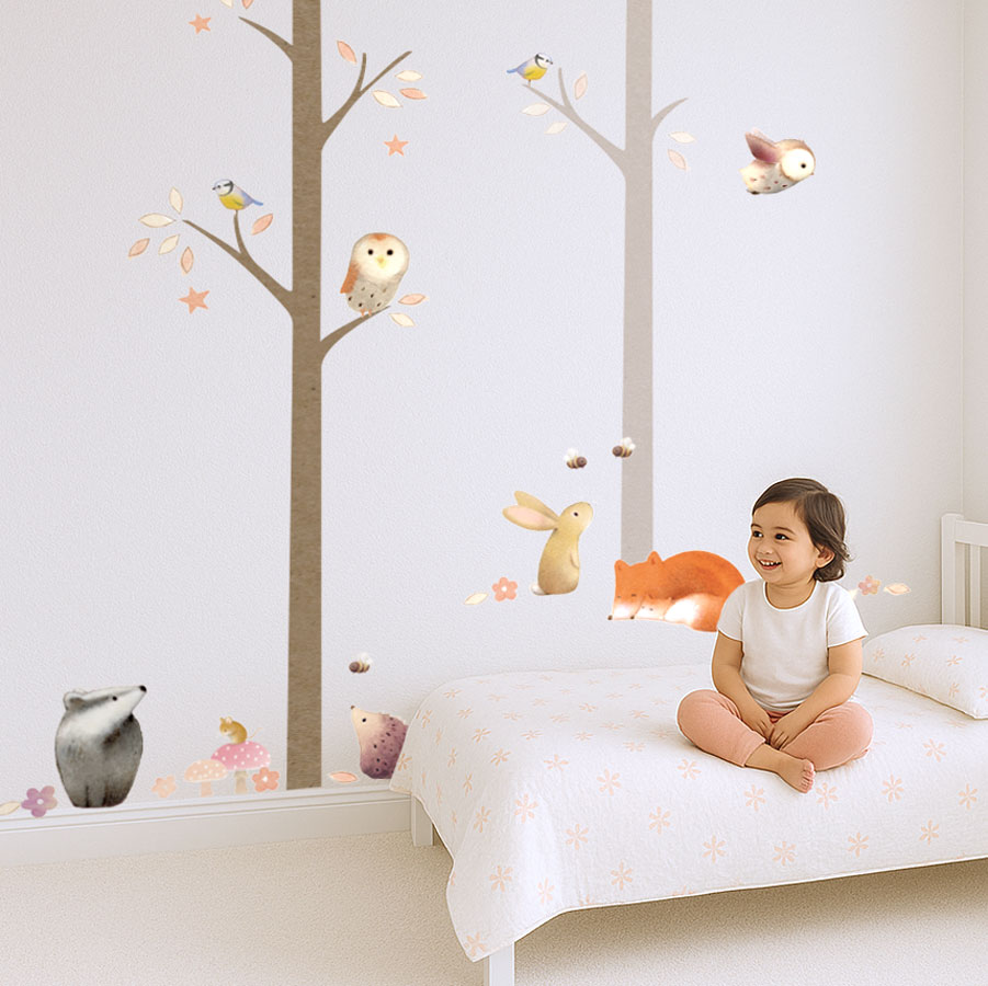 Nursery with woodland wall stickers showing animals and trees from Ginger Betty's Core Pack, with child sitting on bed.