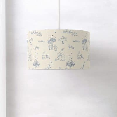Side view of Guess How Much I Love You lampshade with detailed blue line art of hares, trees, and stars on a neutral cream background.