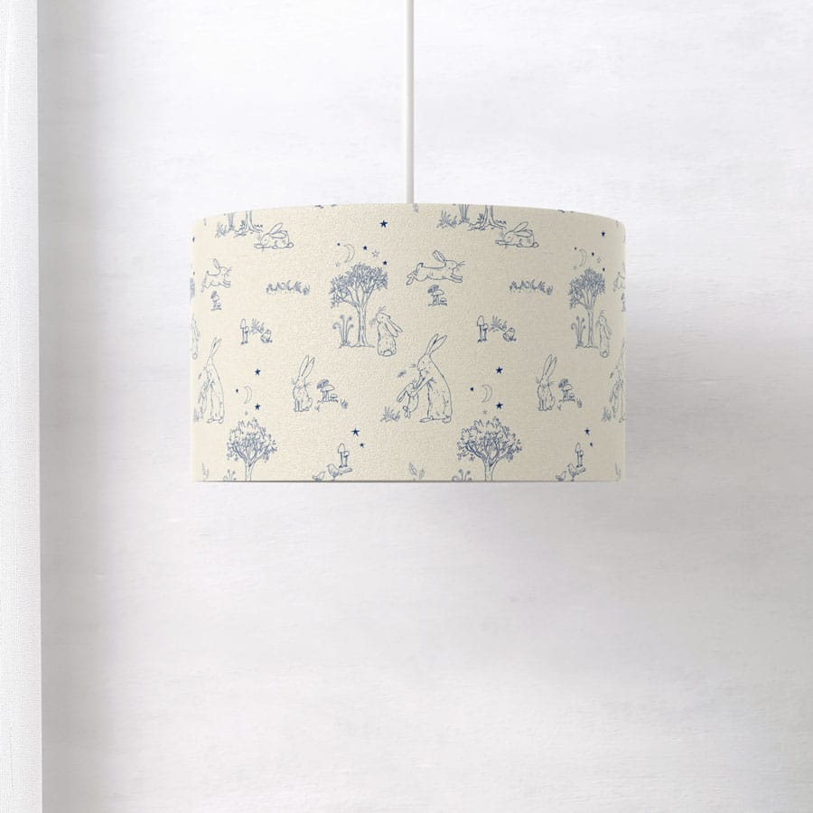 Side view of Guess How Much I Love You lampshade with detailed blue line art of hares, trees, and stars on a neutral cream background.